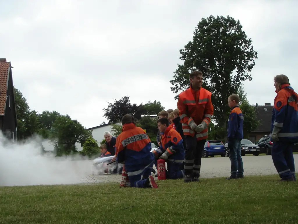 Jugendliche der Jugendfeuerwehr üben mit einem Feuerlöscher, Betreuer schauen zu